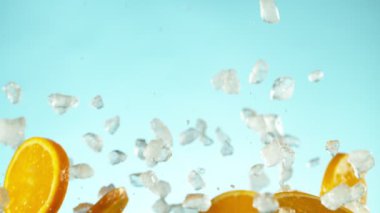 Mavi arka planda ezilmiş buzla birlikte düşen portakal dilimlerinin süper yavaş çekimi. Yüksek hızlı sinema kamerası, 1000 fps..