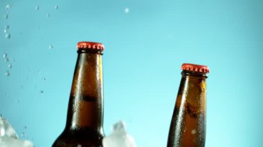 Mavi arka planda buzla birlikte düşen bira şişelerinin süper yavaş çekimleri. Yüksek hızlı sinema kamerası, 1000 fps..