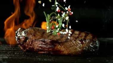 Biftek ızgarada ağır çekimde ve düşen baharatlarla, siyah arka planda. Yüksek hızlı sinema kamerası, 1000 fps.