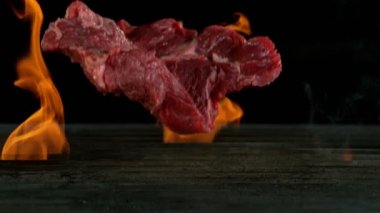 Biftek ağır çekimde ızgaraya düşüyor ve arka planda ateş yanıyor. Yüksek hızlı sinema kamerası, 1000 fps.