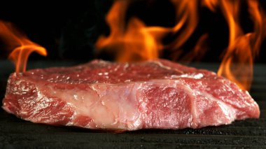 Izgarada çiğ biftek. Pirzola ızgara ızgarasına ateşle konmuş. Siyah arkaplan.