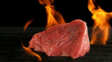 Izgarada çiğ biftek. Pirzola ızgara ızgarasına ateşle konmuş. Siyah arkaplan.