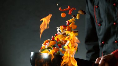 Şefin tavadan sebze karışımını ateşe atmasına yakın çekim. Koyu arkaplanda taze Asya yemeği hazırlığı.