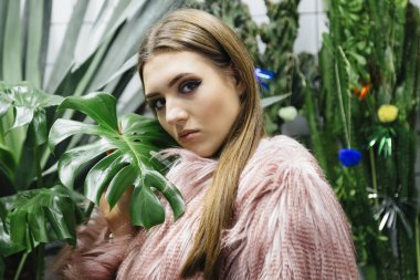 Güzel genç kadın büyük yeşil eco faux kürk beyaz kareli arka plan üzerinde yapraklar.