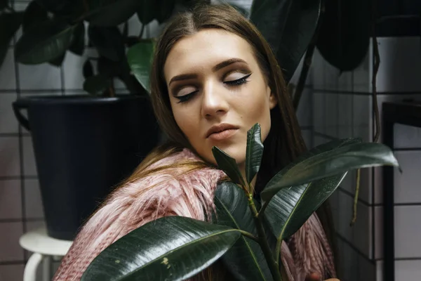 Bella giovane donna con grandi foglie verdi in eco pelliccia cappotto eco su sfondo bianco a scacchi . — Foto Stock