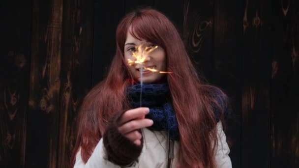 Beautiful smiling ginger young woman stands on a brown background with sparkler at sunset. — Stock Video