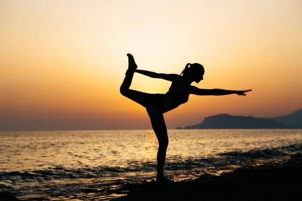 Genç sağlıklı kadın gün batımında plajda yoga yapıyor.
