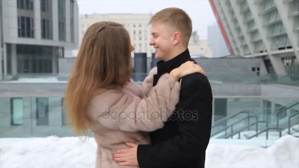 Um jovem heterossexual homem e mulher de casaco de peles casal abraçar e beijar uns aos outros feliz em uma cidade . — Vídeo de Stock