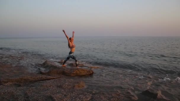 Jeune femme pratiquant le yoga sur la plage au coucher du soleil. — Video