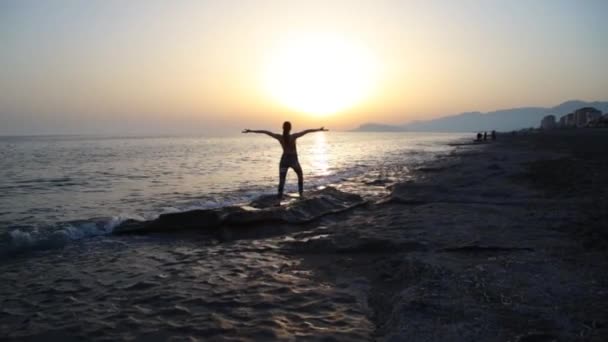 Νεαρή γυναίκα που κάνει γιόγκα στην παραλία το ηλιοβασίλεμα. — Αρχείο Βίντεο