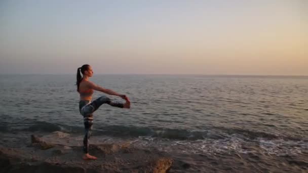 Gün batımında plajda yoga yapan genç bir kadın.. — Stok video