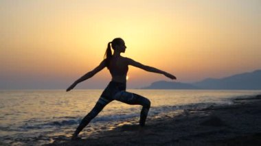 gün batımında sahilde Yoga uygulamak siluet genç kadın.