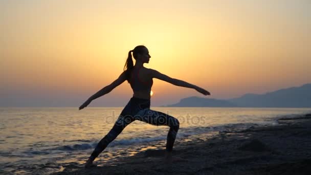 Silhouette junge Frau übt Yoga am Strand bei Sonnenuntergang.