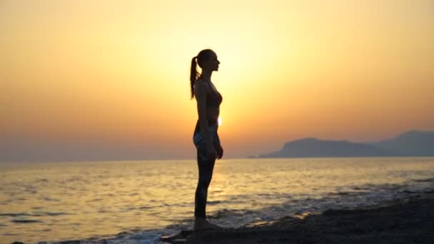 Νεαρή γυναίκα σιλουέτα πρακτική της γιόγκα στην παραλία στο ηλιοβασίλεμα. — Αρχείο Βίντεο