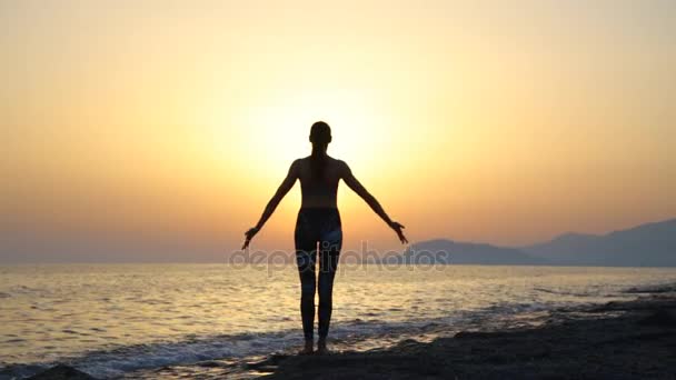 Jonge vrouw silhouet beoefenen van yoga op het strand bij zonsondergang. — Stockvideo