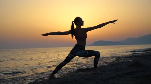 Silhouette ung kvinna utövar yoga på stranden vid solnedgången. — Stockvideo