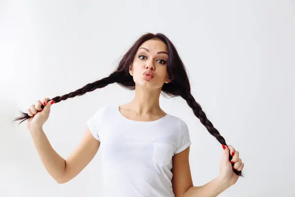 Kırmızı dudaklar kamera öpmek yapmak üfleme genç güzel kadın moda portre. Saç braidspigtails ve beyaz arka plan üzerinde beyaz gömlek giyiyor.