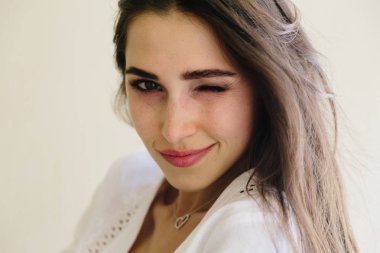 Gülümsemek gülümseyen ve göz kırpıyor mutlu bir genç kadın portresi. Çiller, dalgalı sağlıklı saçlar ile mükemmel cilt.