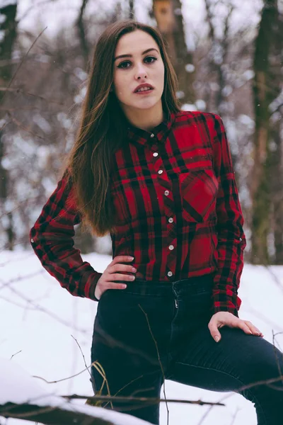 Woman clothed in red checkered shirt in a cold winter snow forest with trees on background.