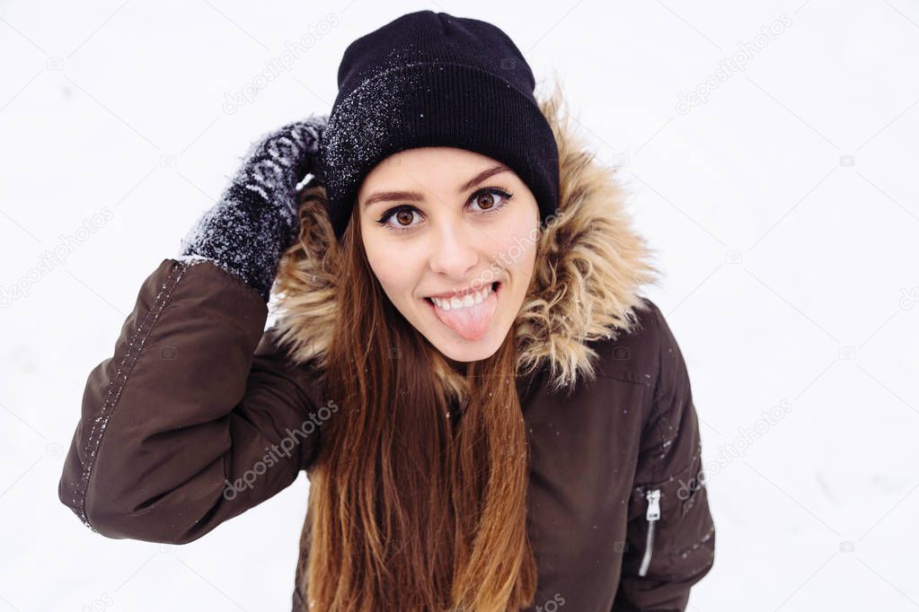 Happy woman warmly clothed in a cold winter snow forest shows tongue at camera.
