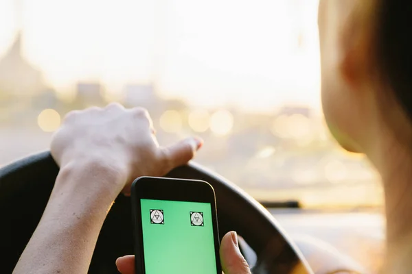 Young female driver using smartphone with Green Screen in a car.