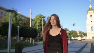 Çekici kız kırmızı dudaklar ile kırmızı paltolu bir şehir sokakta tarafından kamera ve gülümsüyor döner daha gider.