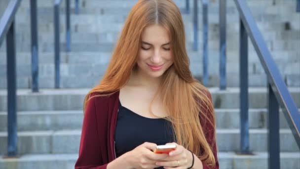 Elegante mooie vrouw met lang haar SMS op smartphone in de stad bij zonsopgang. — Stockvideo