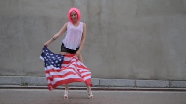 Красивая молодая смешанная расовая женщина в розовом парике с американским флагом на городской улице — стоковое видео