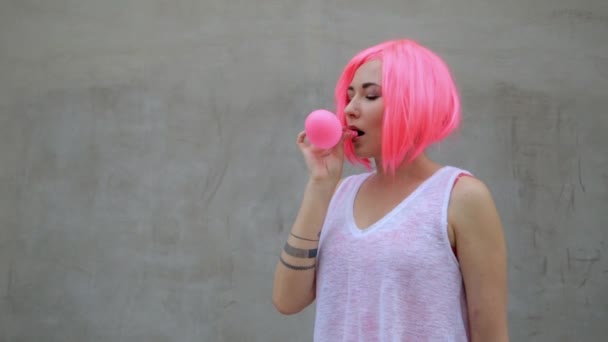 Closeup portrait of mixed race trendy hipster teenage girl blowing a red balloon wearing pink wig — Stock Video