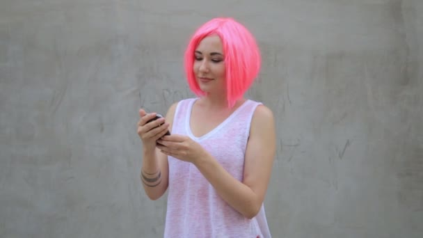 Mooi gemengd ras vrouw in roze pruik SMS sms met behulp van telefoon glimlachend en spinnen genieten van het leven — Stockvideo
