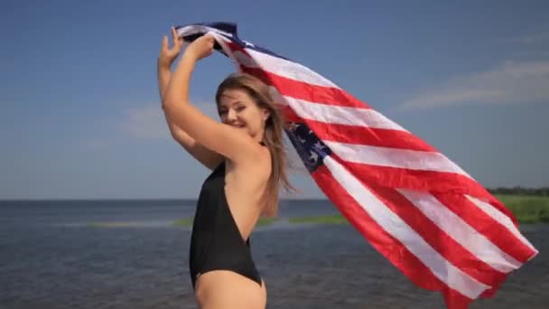 Mooi slank meisje in bikini genieten van leven aan het volledige dansen op het strand met Usa vlag — Stockvideo
