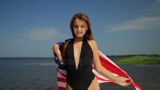 Menina fina bonita em biquíni desfrutando de vida para a dança completa na praia com bandeira dos EUA — Vídeo de Stock