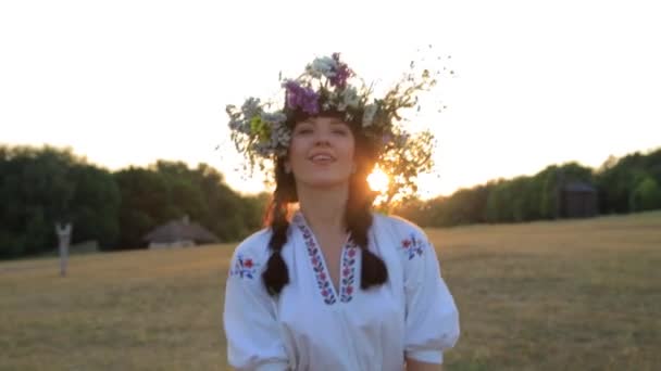 Ragazza che cammina nel prato indossando cerchio di fiori e abiti etnici al tramonto in natura — Video Stock