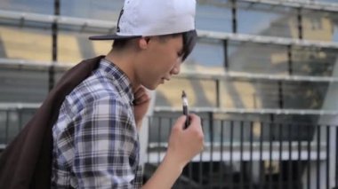 Üstünde belgili tanımlık sokak ve duman E-Sigara yürüyen genç adam. Vape