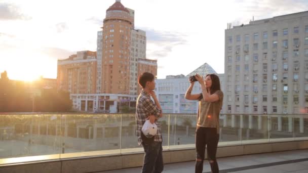 Estudante asiático posando para uma menina de raça mista fotógrafo ao ar livre na cidade. Nos bastidores da sessão fotográfica — Vídeo de Stock