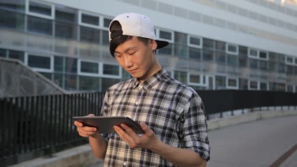 Молодий азіатський чоловік у місті використовує планшетний комп'ютер на відкритому повітрі — стокове відео