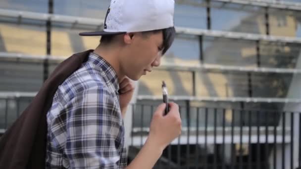 Un joven caminando por la calle y fumando cigarrillos electrónicos. Vape. — Vídeos de Stock