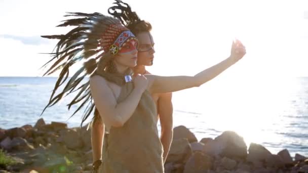 Ung leende Native American indian man och kvinna i bohemiska stilen solen bära klänning tar selfie på stranden vid solnedgången — Stockvideo