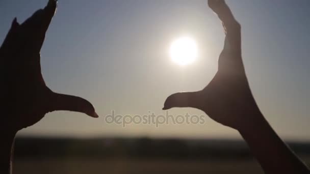 Donna irriconoscibile che prende il sole al tramonto con le dita a forma di cuore. Giovane ragazza che fa il simbolo dell'amore con le mani contro il sole mattutino sorprendente — Video Stock