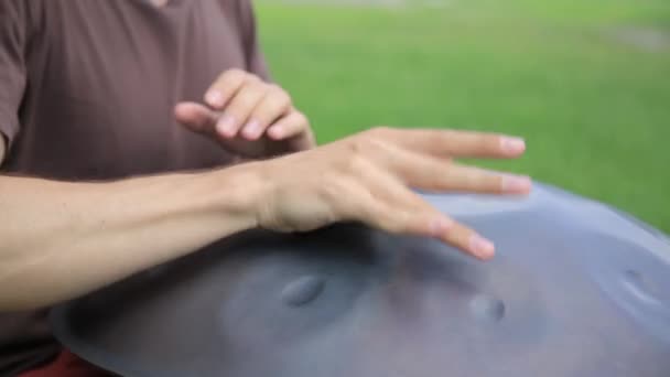 Pemain drum beraksi. pria duduk di rumput dan bermain handpan atau menggantung drum . — Stok Video