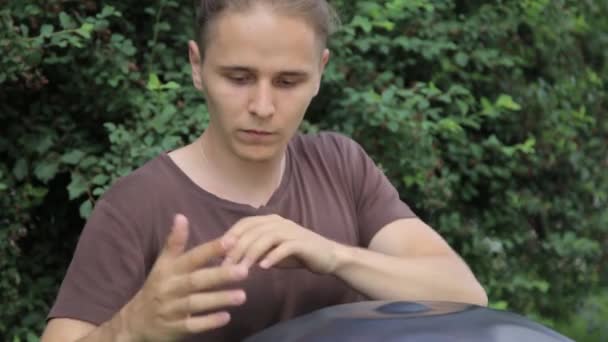 Le batteur en action. gars assis sur l'herbe et jouer du handpan ou accrocher le tambour . — Video