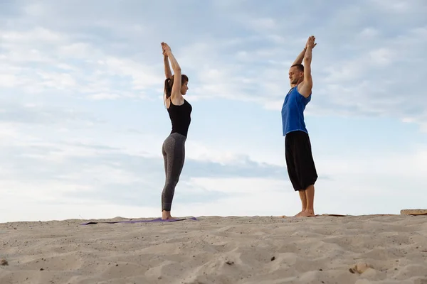 Erkek ve kadın çölde gün batımında yoga yaparken gençler.
