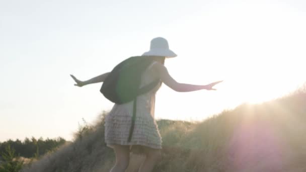 Mulher turística em belo vestido e mochila andando no topo de uma montanha e olhando para o horizonte. Experiência de viagem ao pôr-do-sol, menina desfrutando de um estilo de vida relaxado nas férias de verão — Vídeo de Stock
