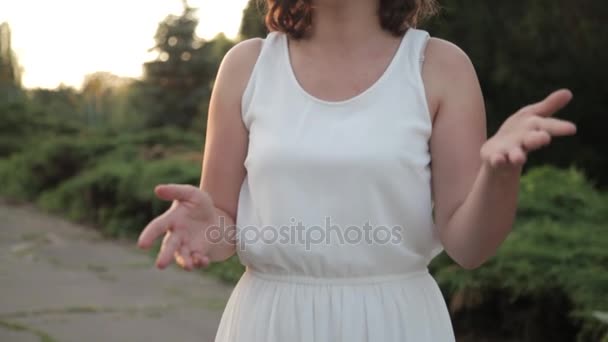Menina bonita nova com flor circlet e vestido branco canta e dança ao ar livre ao pôr do sol — Vídeo de Stock