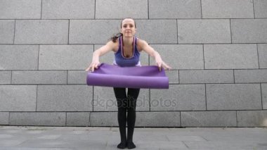 Kadın apart yoga mat gri Kentsel şehir arka plan üzerinde kamera alır. Özgürlük, sağlık ve yoga kavramı. Atış kapatın