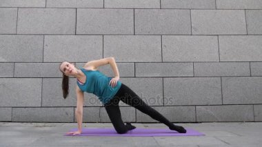 Genç kadın yoga yaparken spor ve kentsel arka plan ve pembe yoga mat pilates fitness egzersizleri üzerinde gri