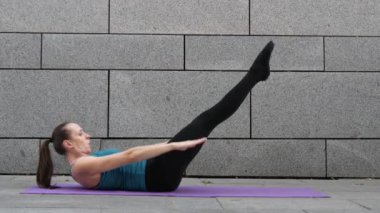 Genç kadın yoga yaparken spor ve kentsel arka plan ve pembe yoga mat pilates fitness egzersizleri üzerinde gri