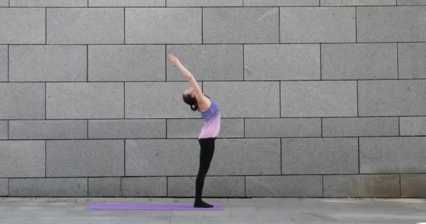 Mujer practica ejercicio de yoga fitness sobre alfombra rosa en la ciudad sobre fondo urbano gris — Vídeo de stock