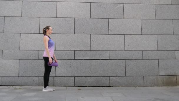 Mujer rueda aparte estera de yoga sobre fondo gris ciudad urbana. Concepto de libertad, salud y yoga. Primer plano. — Vídeos de Stock