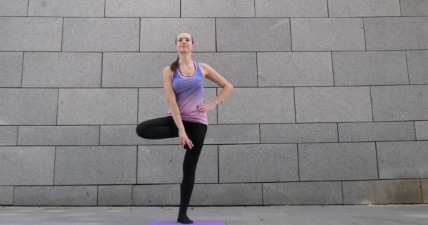 Mujer practica ejercicio de yoga fitness sobre alfombra rosa en la ciudad sobre fondo urbano gris — Vídeo de stock